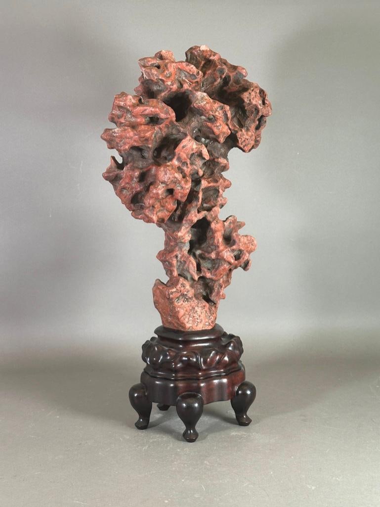 Chinese Carved Stone Scholar's Rock in Stand: Chinese Carved Stone Scholar's Rock in Stand, carved in red stone emblematic of a spiritual cloud form for contemplation. In fitted wood stand. Dimensions: 22 in.h. x 10 in. w x 7 in.d. Condition: Two