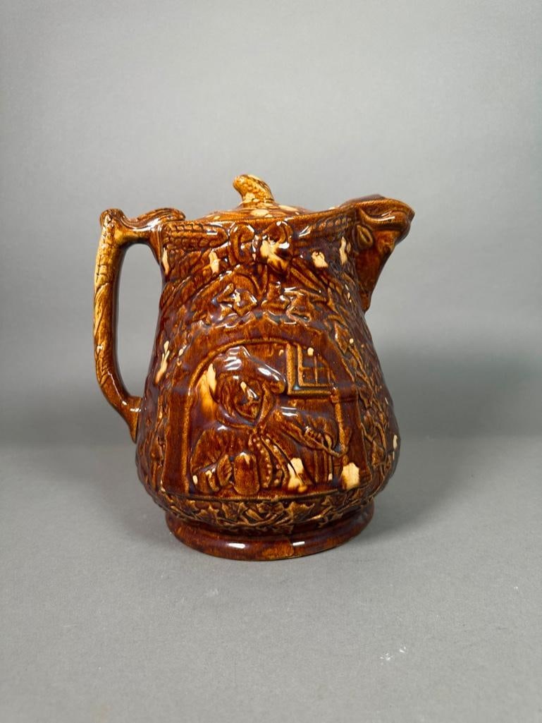 Rockingham Ale Jug, Tavern Scene: Rockingham Ale Jug, Tavern Scene, baluster form jug in speckled brown glaze, with wheat sheaf handle, the body molded with a tavern scene with a man enjoying a mug of ale and a pipe, with molded bull