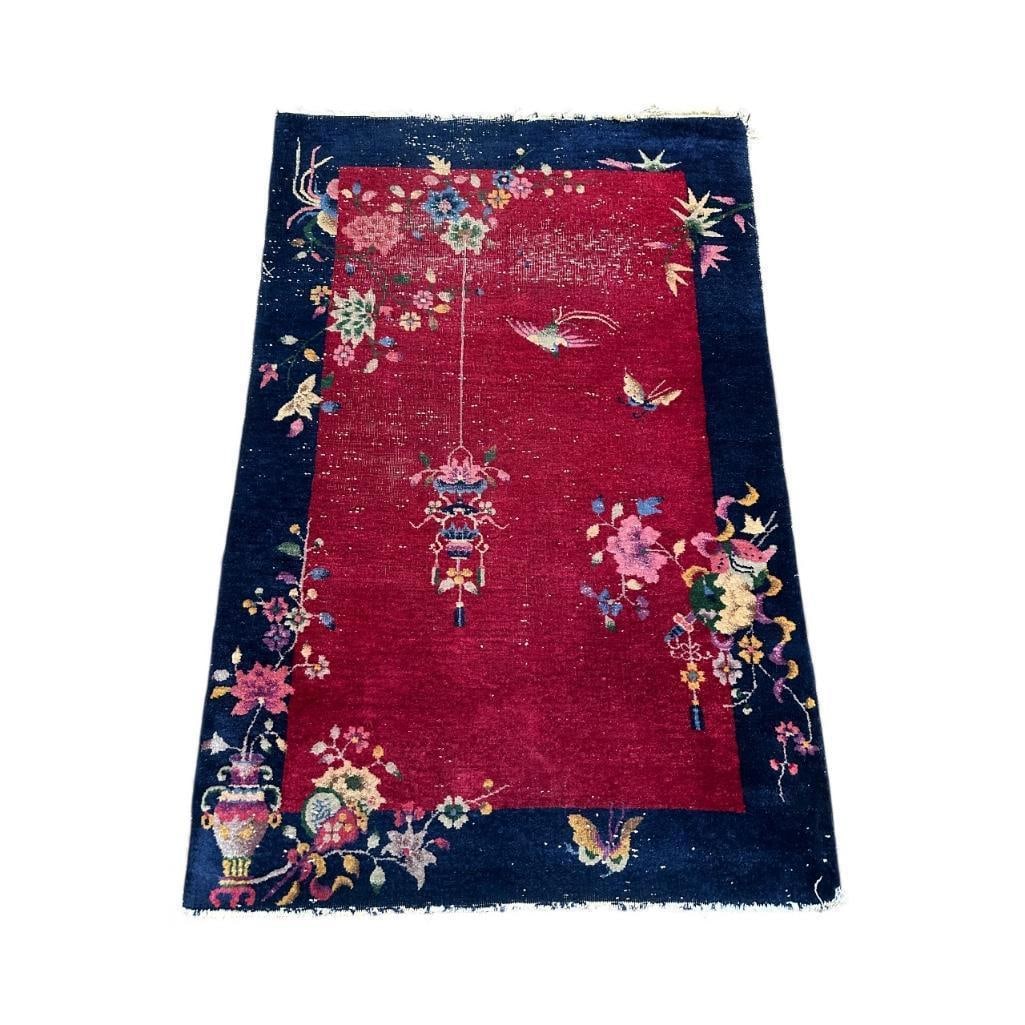 Chinese Art Deco Carpet 6' x 4': Wool on cotton weft, cherry red ground with dark blue wide border. Directional carpet with hanging lantern, a vase with flowers at lower left, and butterflies throughout with flowers. Short fringe end
