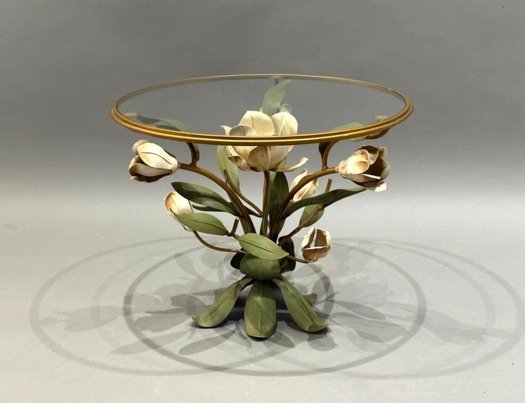 A Tole Peinte Table with Glass Top, Modern: A Tole Peinte Table with Glass Top, Modern. Circular top with clear glass over a base fashioned as magnolia leaves and blossoms in green and white, with gold framework. Dimensions: 17.5 in.h. x 22 in.