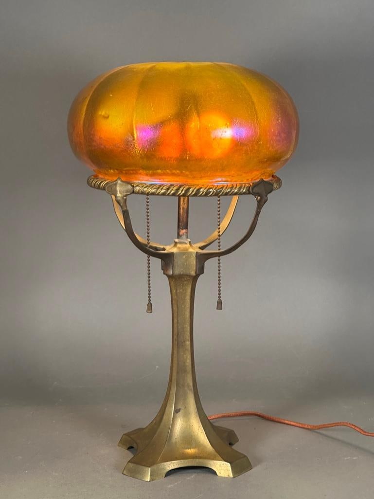Art Nouveau Table Lamp with Iridescent Glass Shade: Art Nouveau table lamp with unsigned iridescent shade. Lamp with two pull chains with tassel ends, wired for electricity, four arms hold a circlet which the base of the shade rests upon. Under the