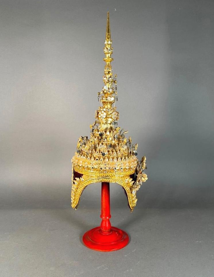 Thai Ceremonial Headdress: That Ceremonial Headdress, gilde papier mache tiered crown with mirrored pendant decorations, on red painted wood stand. Dimensions: 26 in.h. Condition: Dust accumulations. Some pieces bent.