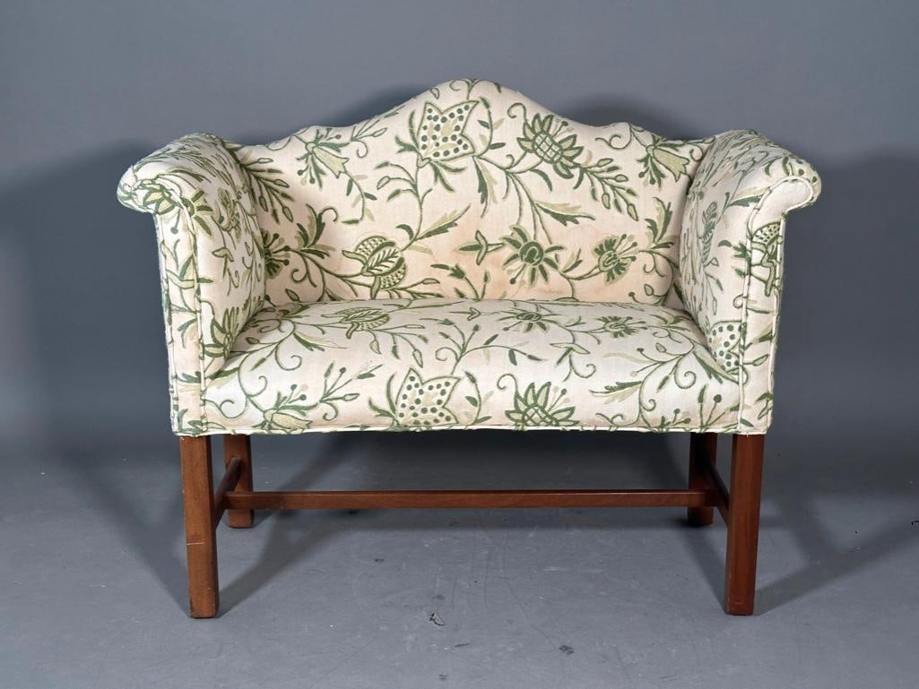 Crewel Upholstered Camel-back Settee: Petite camel-back settee, upholstered in wove cotton cloth, with crewel-work stitching wool in various shades of green. Mahogany wood base with stretcher, tag on bottom from the Berkely Upholstery
