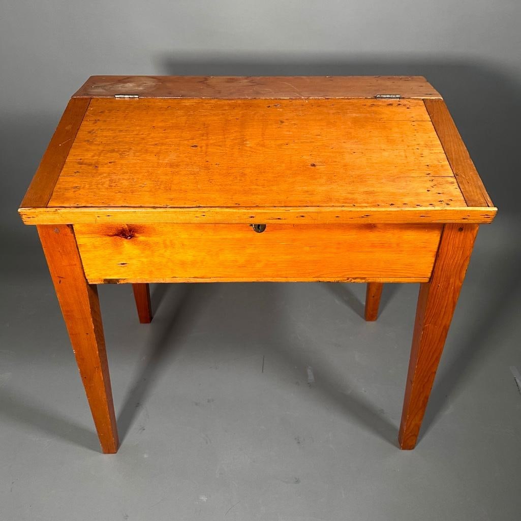 School Master's Slant-front Desk, 19th century: American pine writing desk with hinged slant-front, opening to a deep compartment with smaller compartments, raised on plain tapering legs. Apprx 32 x 33 x 23 inches. Condition: newer varnish,