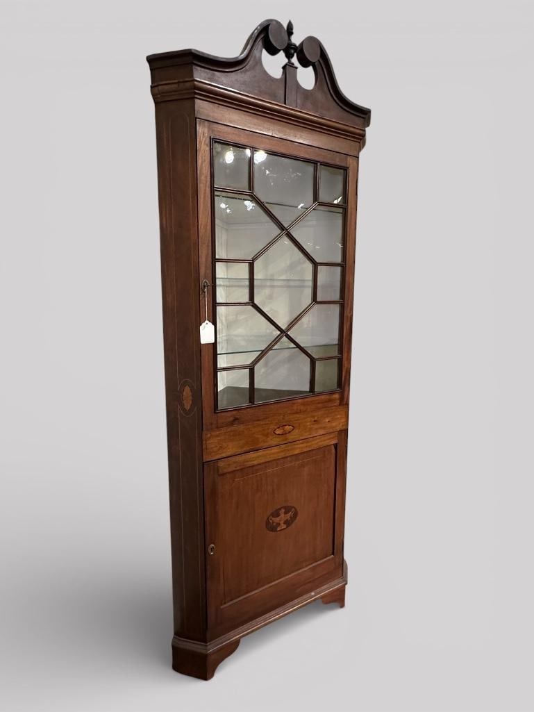 Antique Federal Style Corner Cabinet: An inlaid antique Federal Style mahogany corner cabinet with swan neck and flame finial crown. Inlaid with satin-wood scalloped cartouches on the front and sides, lower door exhibits inlaid