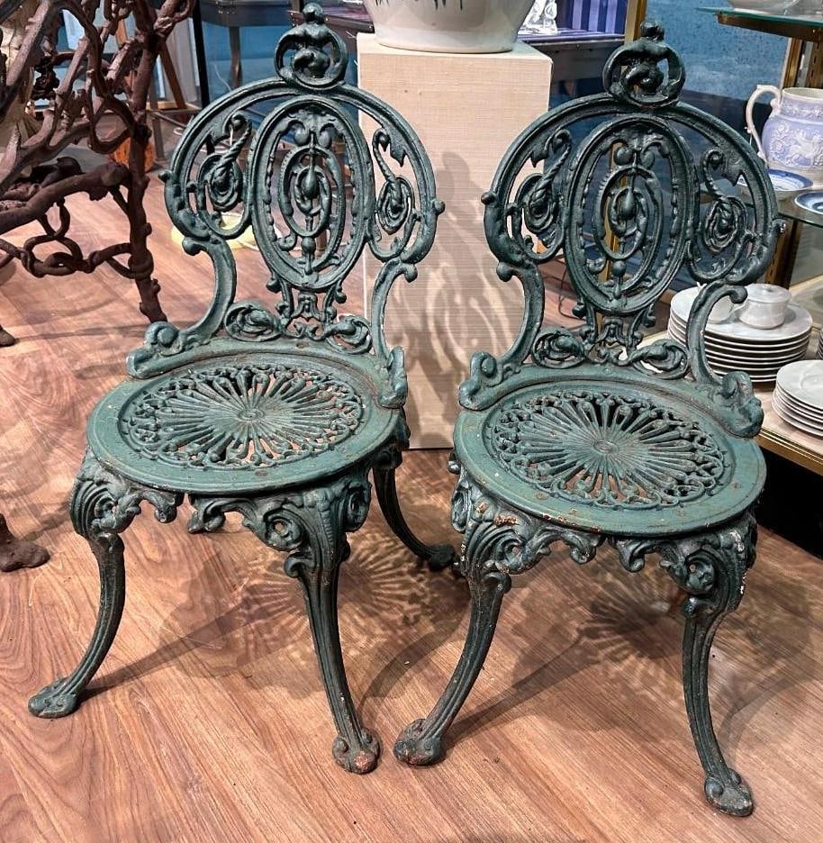 Pair of Victorian Cast Iron Green Painted Garden Chairs: Pair of Victorian Cast Iron Green Painted Garden Chairs, diminutive forms cast with cartouche shaped backs over a stylized floral medallion seat, on downswept legs. Dimensions: 31 in.h. x 14.5 in.w. x