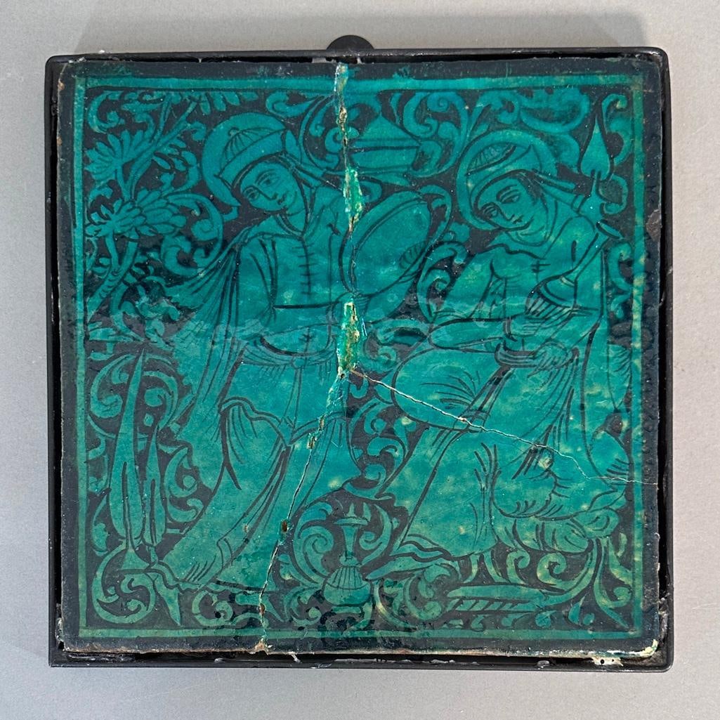 Antique Persian Turquoise Glazed Ceramic Tile: Antique Persian Turquoise Glazed Ceramic Tile, fitted in metal frame, depicting figures in flowing robes, one holding a vase, the other with a bowl form, another vase at their feet, reserved on a foli