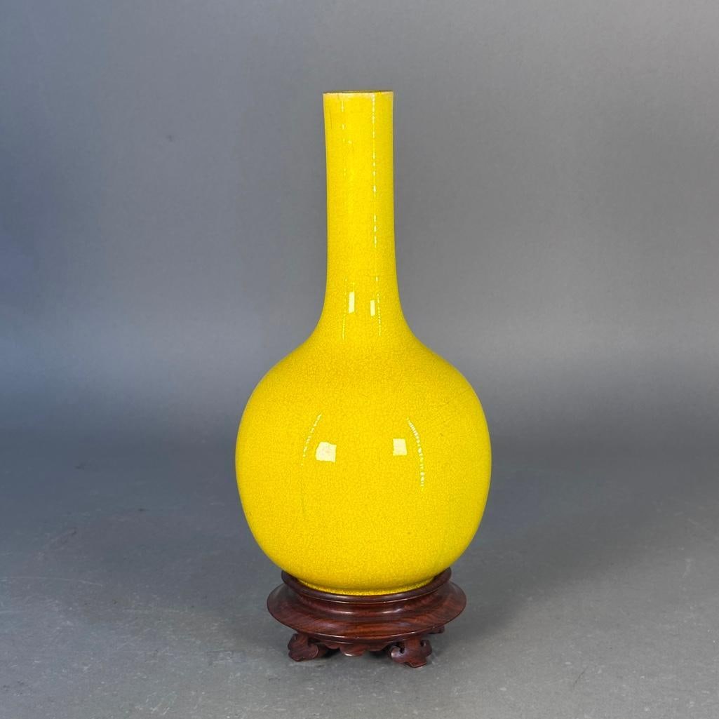 Chinese Monochromatic Bottle Vase, ca. late 19th century: Chinese vase, yellow high fired glaze with craquelure on small foot, unsigned or marked, with carved wood stand; vase measures 10.25"T. Condition: crazing to glaze, the rim has wear with two small