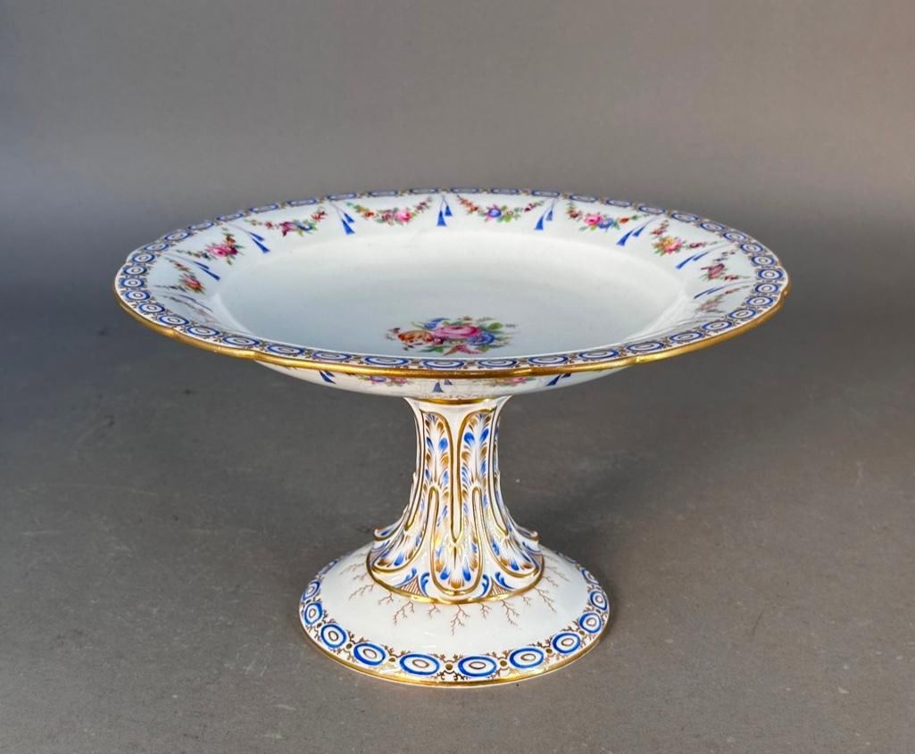 Sevres Style Porcelain Tazza, c. Early 20th century: Porcelain centerpiece or compote, hand decorated and gilt in beautiful cobalt blue and gold; the bowl has a lovely border with a rose garland swag and floral bouquet center, raised on a sculptural ped