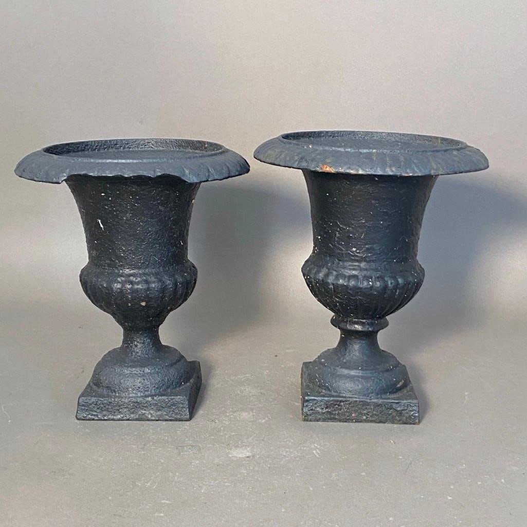 A Pair of Small Cast Iron Garden Urns: Cast Iron, painted black, reverse bell shape with gadrooned bottom, raised on squared domed base. Dimensions: Each apprx. 10"T x 8-.5"D. Condition: both have a substantial chipped rim. Soils f