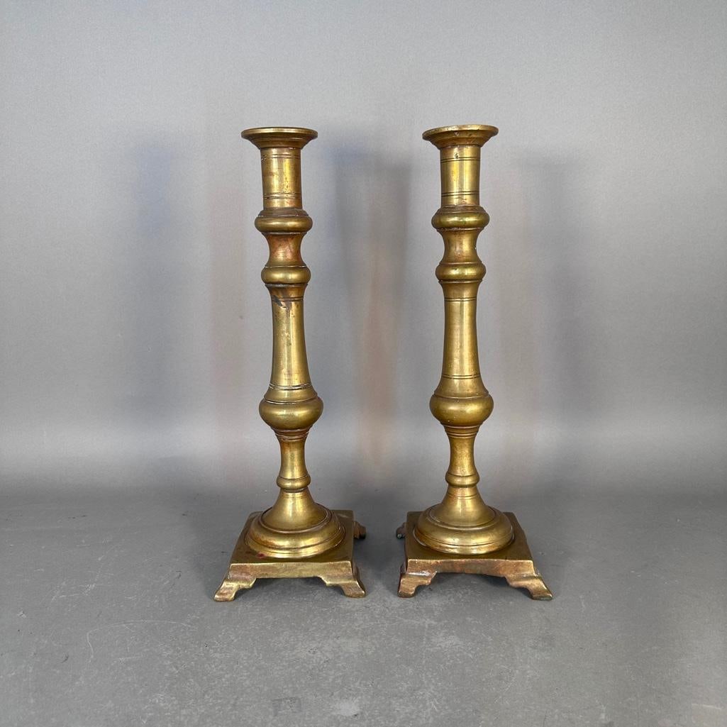 Pair of Monumental Brass Candlesticks: Pair of large, knoped, stem candlesticks raised on squared, footed base. Brass. Apprx. 6 in.l x 6 in.w x 18 in.h. Condition: wax residues, good.