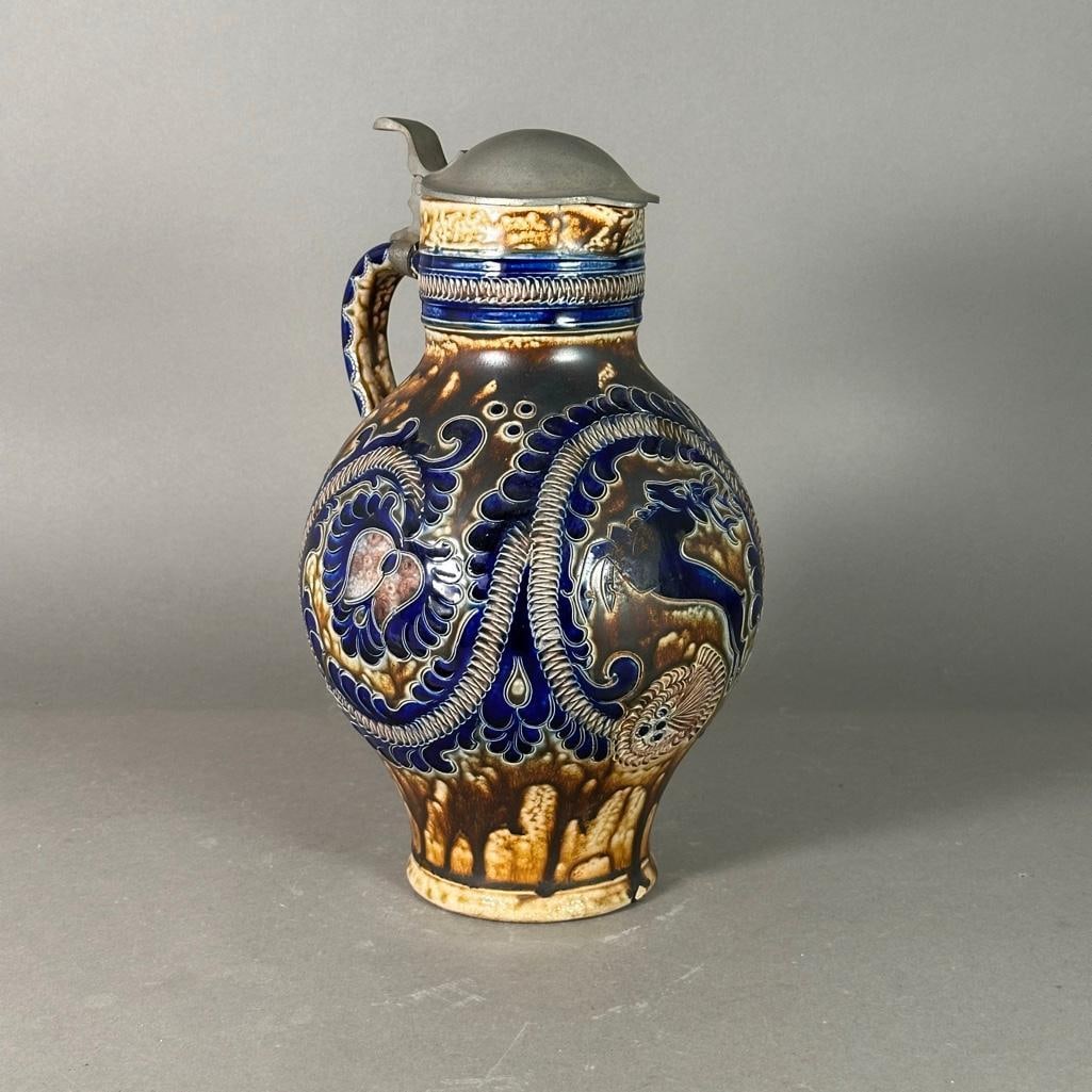 Reinhold Merkelbach Wine Pitcher: Stoneware pitcher with tin lid, incised decorations, a leaping deer on the front, finished in a salt glaze of brown and cobalt blue with a high fired finish. Impressed markings on bottom, made in west