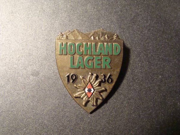 GERMANY NAZI 1936 HOCHLAND LAGER BADGE. RARE.: OUTSTANDING 1936 HITLER YOUTH "HOCHLAND LAGER" BADGE. IN BRONZE WITH GREEN ENAMEL LETTERING, BLACK ENAMEL DATE AND HJ SYMBOL. SHIELD SHAPE WITH MOUNTAINS ON TOP. THERE IS A RAISED EDELWEISS WITH ENAME