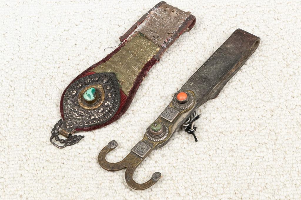TWO CENTRAL ASIAN DECORATED LEATHER STRAPS: TWO CENTRAL ASIAN DECORATED LEATHER STRAPS WITH TURQUOISE AND CORALOne leather and fabric belt end with silver metal appliqu with a monster face and a buckle. Turquoise cabochon detail. L. 10 3/4", W.