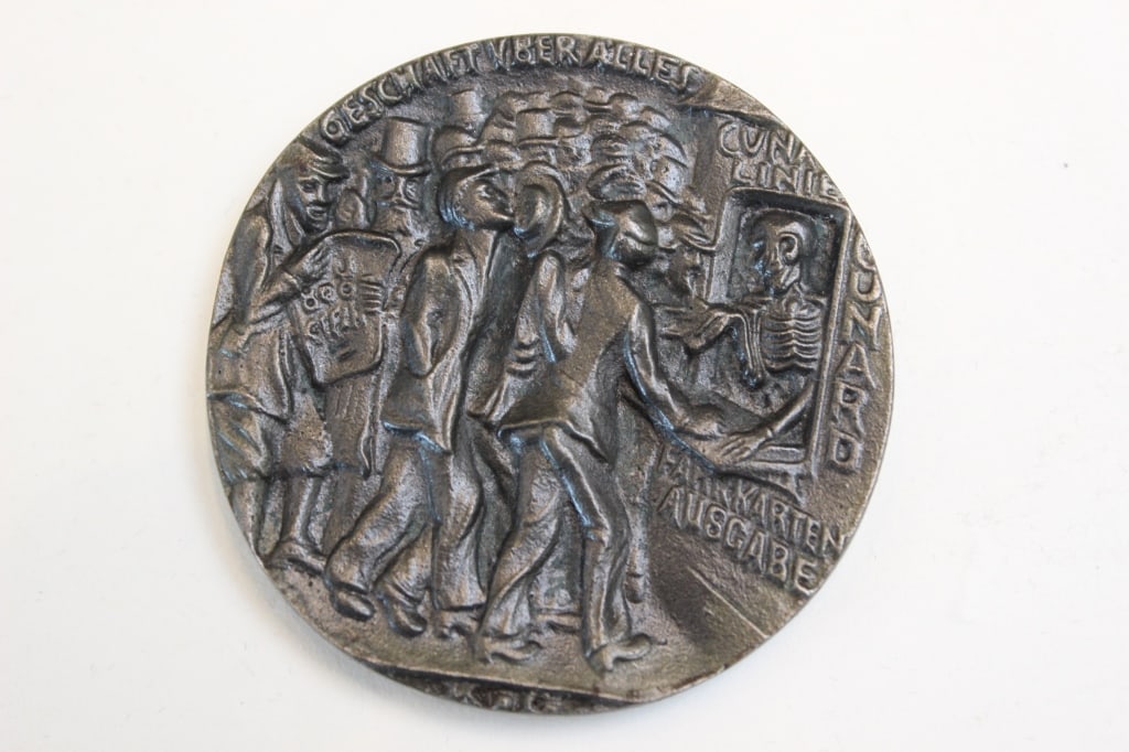 Lusitania medallion, British issue: Dimension: 2 1/8"W. The medallion obverse depicts, in high relief, the SS Lusitania sinking with war cargo spilling from her deck. Around the top edge are the words 'KEINE BANN WARE' (No contraband go