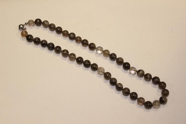 Beaded Quartz Necklace: The necklace features beads that vary in color from a clear, colorless quartz (rock crystal) to a dark, translucent brown, characteristic of smoky quartz. Many of the beads also contain fine, needle-l