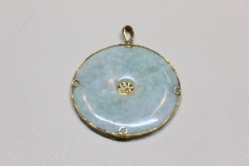 Vintage 14K yellow gold and Jadeite Pendant: vintage 14K yellow gold and light green (celadon) jade "Bi" disc pendant featuring the Chinese character for "good fortune".The central stone is a flat, round, donut-shaped piece of polished light gre