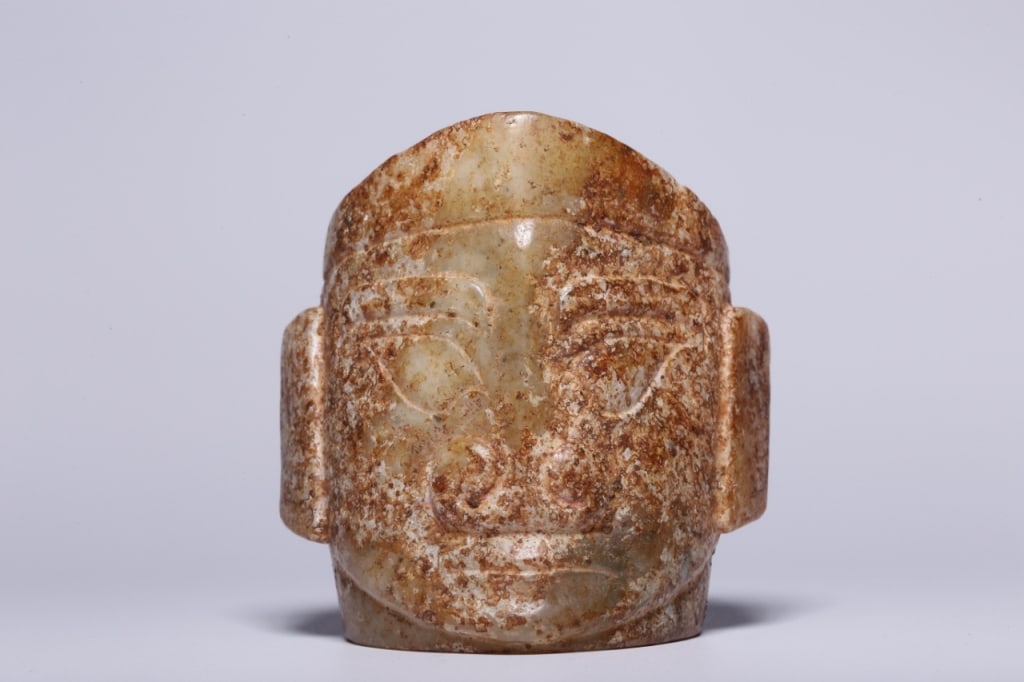 Archaistic Chinese Jade Carved Human Face: Dimension: 6.7cm L x 6cm It is a carved, mask-like human head with stylized facial features including deep-set eyes, a prominent nose, and large ears. It is likely designed as a pendant, as similar ex