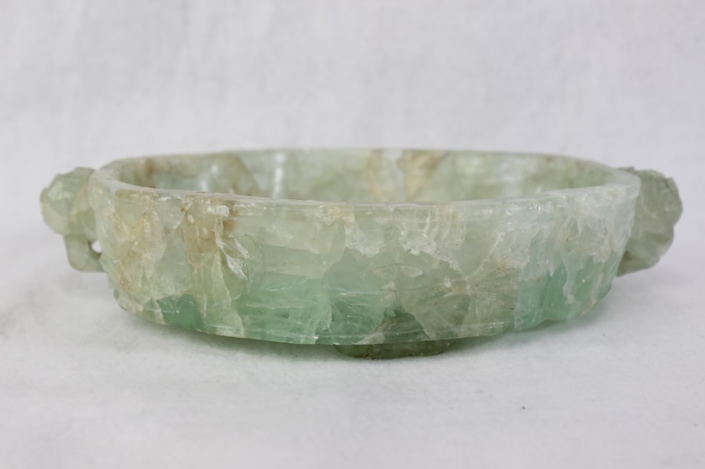 Hand-carved Green fluorite stone Planter: Dimension: 9 1/2"x 6 1/2". \The piece is characterized by an organic, natural shape with some visible veining and fracturing that are inherent to the stone. There appear to be stylized "handles"