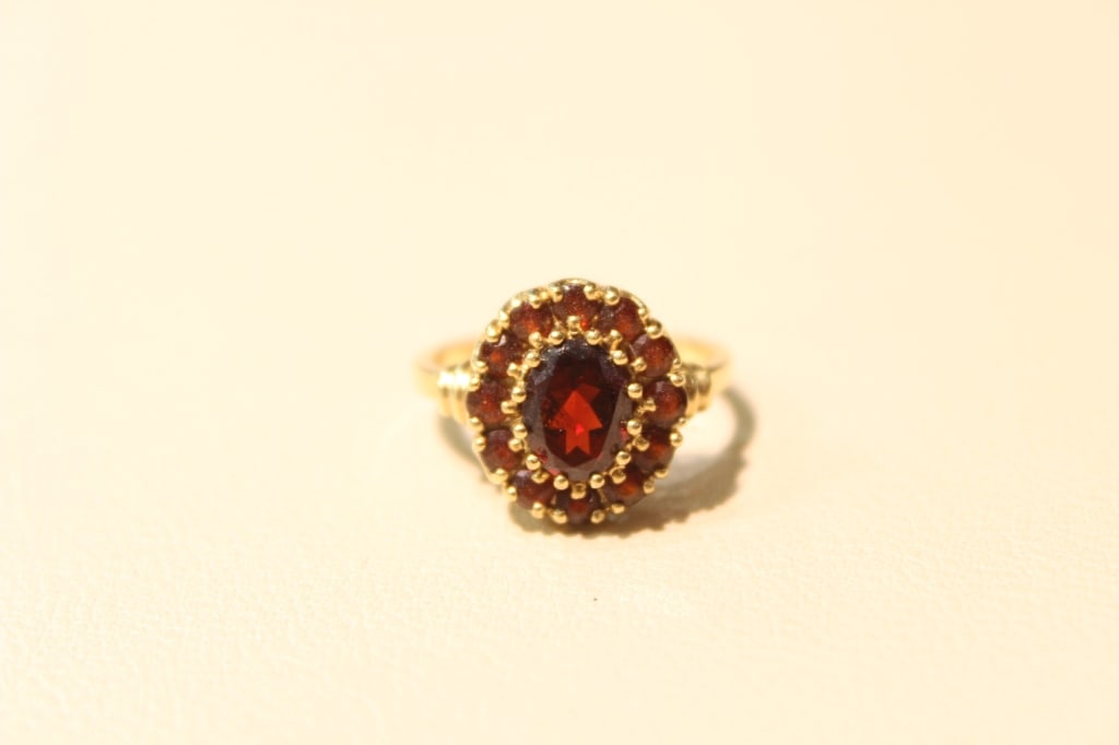 Vintage 10K Gold Oval Garnet Cluster Ring: a style characterized by deep red gemstones set in a flower-like "halo" or tiered cluster arrangement. This specific piece features a large oval-cut central garnet surrounded by a halo of smaller