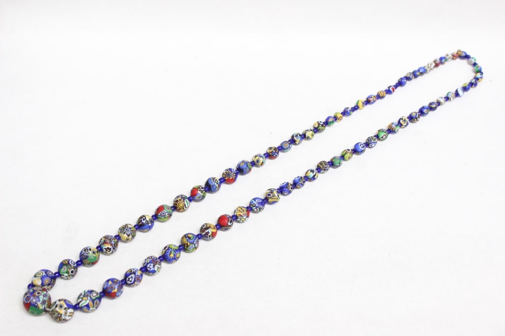 Murano Millefiori Glass Bead Necklace: Each bead is created using the murrine technique, where sections of multicolored glass canes are fused and shaped. The beads are typically separated by small blue glass spacer beads . 18 1/2"L .