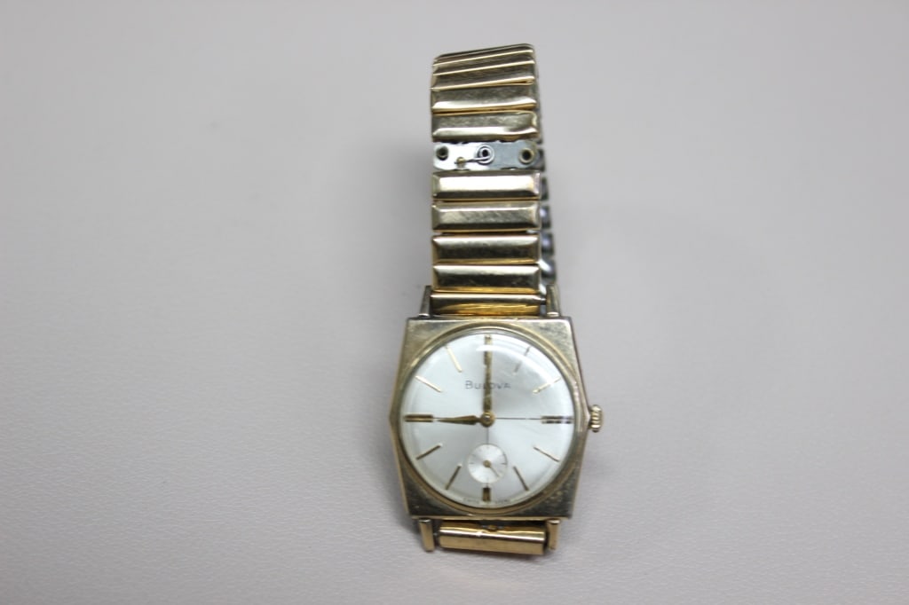 vintage Bulova manual-wind wristwatch: Features a silver sunburst finish with a sub-seconds dial at the 6 o'clock position, a hallmark of mechanical watches from the mid-20th century. The hour markers are gold-toned applied batons. It is f
