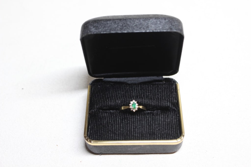vintage emerald and diamond cluster ring: The ring features a central round-cut green emerald surrounded by a "halo" of small white diamonds. The stamp inside the band reads "14K PEMA": PEMA: This is the maker's mark for PEMA Diamonds,