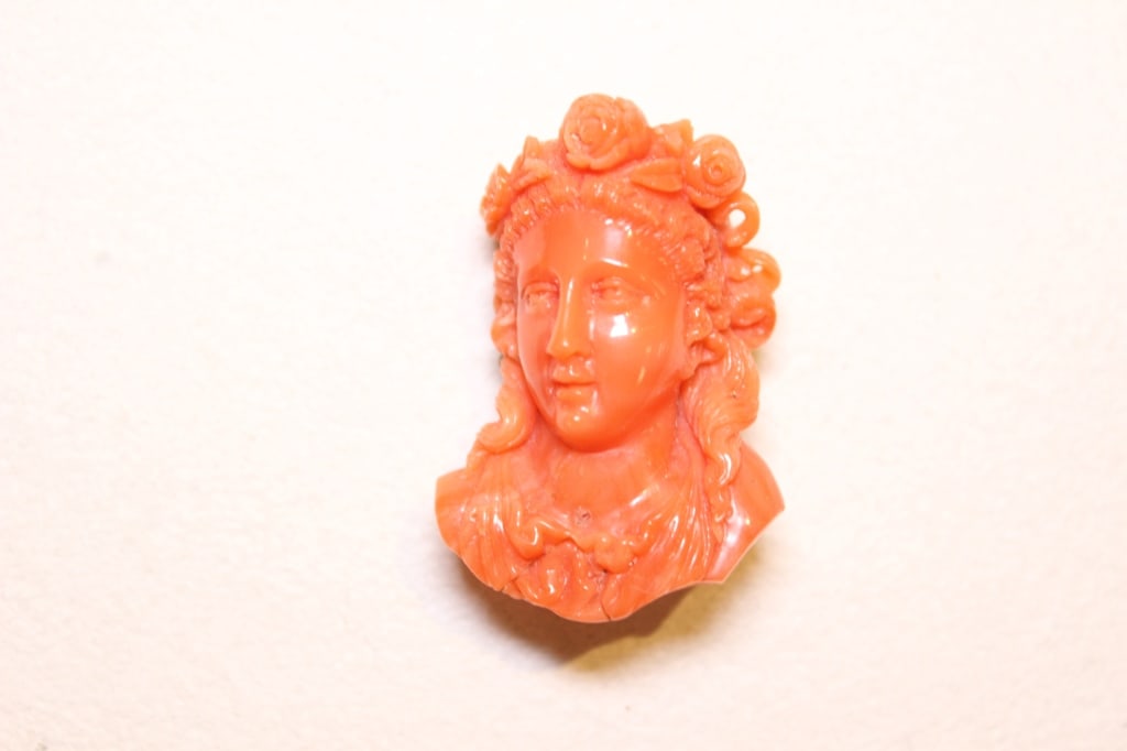 High-relief Hand-carved Coral Cameo Bust Brooch: Dimension: 1 1/2"x 1"W. It depicts a woman (often a goddess or bacchante) in a neoclassical style, featuring a detailed hairstyle adorned with three carved roses.