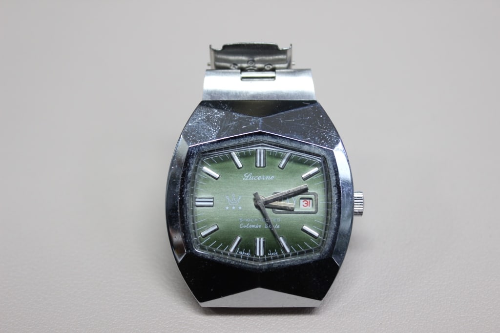 Vintage Lucerne "Colombo Style" wristwatch: It features a distinctive faceted tonneau (barrel-shaped) case with an integrated metal bracelet, typical of the bold, geometric watch styles of the 1970s. The face has a vibrant green sunburst dial