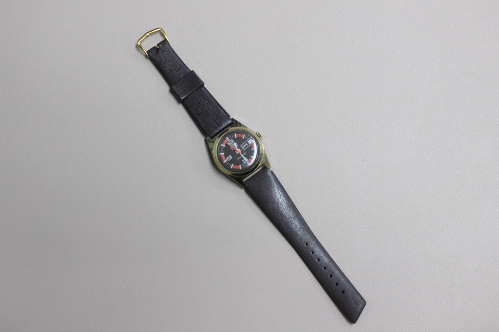 Vintage Stacy "Super 21" Antimagnetic wristwatch: The dial has a high-contrast black and orange "racing" design with an inner minute track in orange. Large Arabic numerals are used at 12 and 9, with a date window prominently displayed at the 3