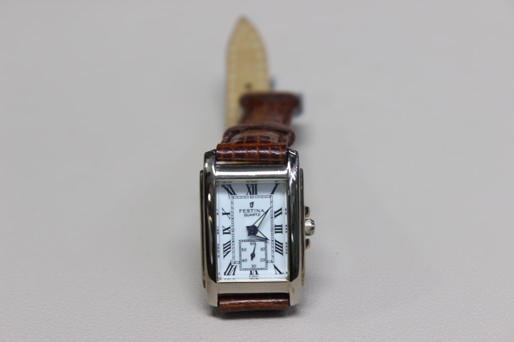 Festina Quartz "Tank" style wristwatch: Its rectangular design is a classic "homage" to the famous Cartier Tank. It features a polished stainless steel rectangular case with a white "art deco" dial, black Roman numerals, and a railway
