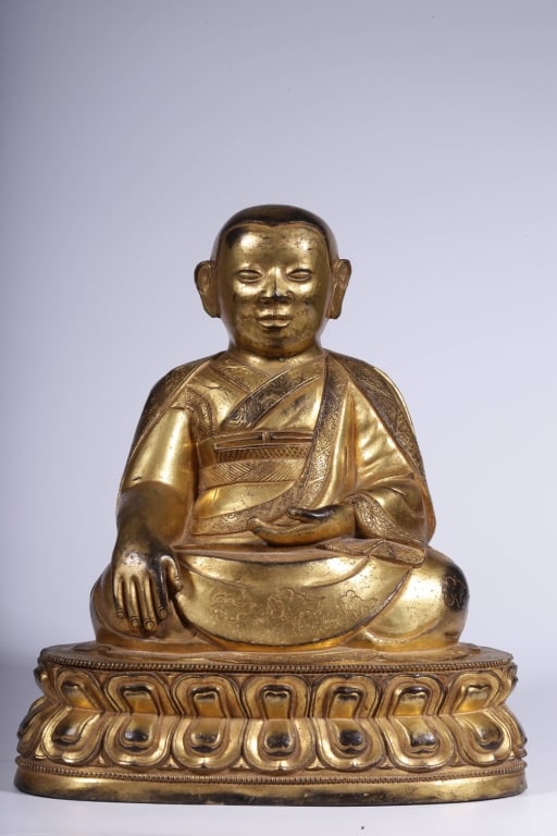 Tibetan Gilt-bronze Statue of a Lama: depicted in a seated meditative posture upon a double-lotus pedestal. Dimension : 23cm H x 20cm L x 15cm,weight is 4323gram. He wears the traditional layered monastic robes of