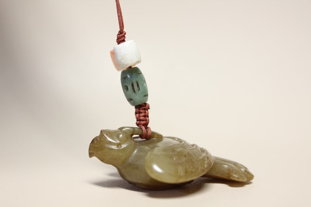 Chinese bird-shaped jade Pendant: Dimension:2 1/4"x 1 5/8". The carving represents a resting predatory bird, likely a hawk, eagle, or falcon. It is defined by a sharply hooked beak, large stylized circular eyes, and a prominent crest 