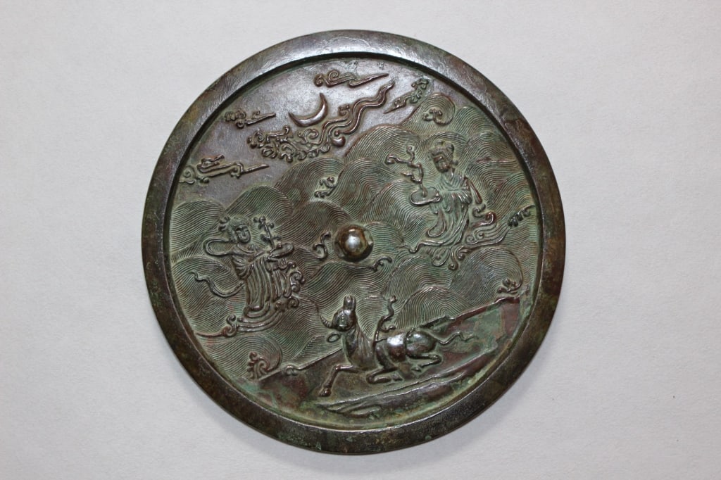 Chinese Relief-carved Bronze Mirror.: Chinese Bronze Mirror. Dimension: 7 3/4"W. At the bottom sits a horned ox or rhinoceros resting on a riverbank, its head turned upward toward the sky. Two floating robed figures (immortals or