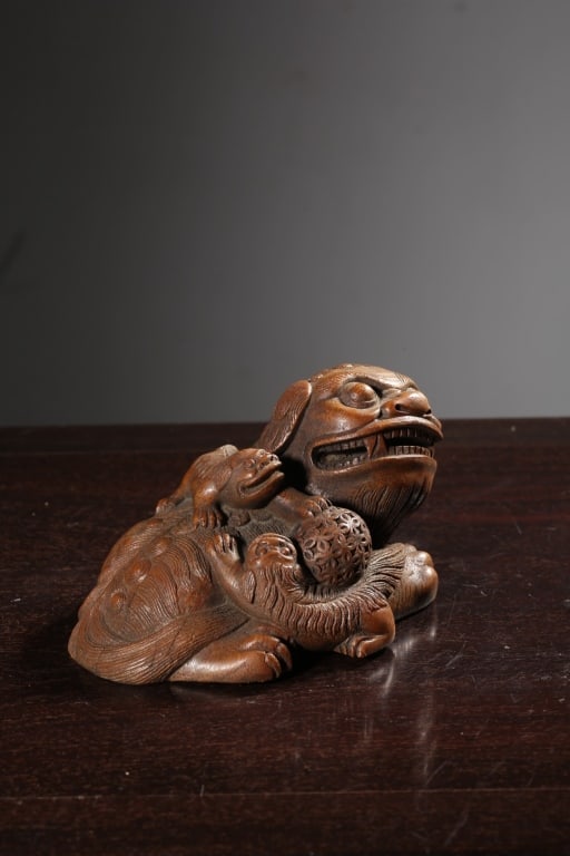 Chinese hand-carved bamboo Guardian Lion with cubs: Dimension: 14cm L x 10cm x 8cm H/. a guardian lion resting on its belly with its head turned to the side. It has a fierce yet playful expression, complete with wide, bulging eyes, a broad nose, and an