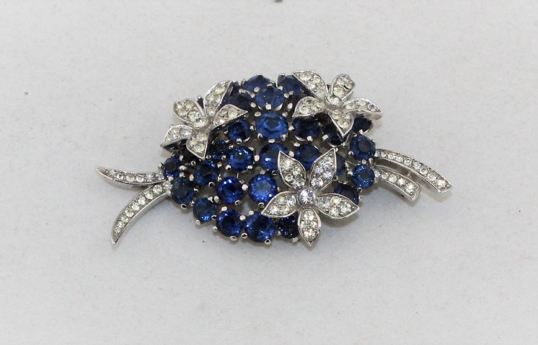TRIFARI Sapphire Blue Rhinestone Brooch Pin: Beautiful TRIFARI sapphire blue and crystal clear rhinestone brooch, in the shape of a bridal bouquet, marked with a crown over the T in Trifari. All of the rhinestones have no foil backs, the metal i