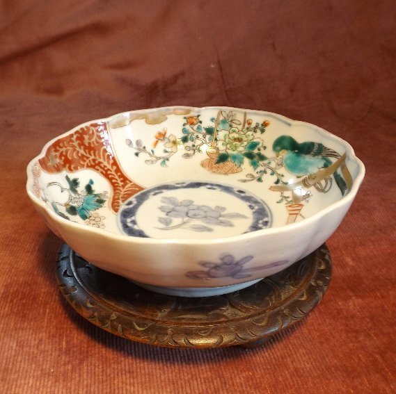 Japanese Imari Bowl, Meiji Period 1880s wooden stand: Antique hand painted imari porcelain bowl on hand carved wooden stand. Scalloped bowl with blue green bird, wine, flowers and gold decoration. The reddish brown wooden stand has hand carved flowers on
