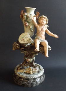 Large Porcelain Sculpture Cupid Amor, Vase, 1880s German Belle Epoque: Large antique Belle Epoque era German porcelain sculpture 'Singing Cupid' [Eros, Amor], with vase, 1880s a complex multi-part work, underglaze hand painted. Cupid is sitting on a stand carried by thre