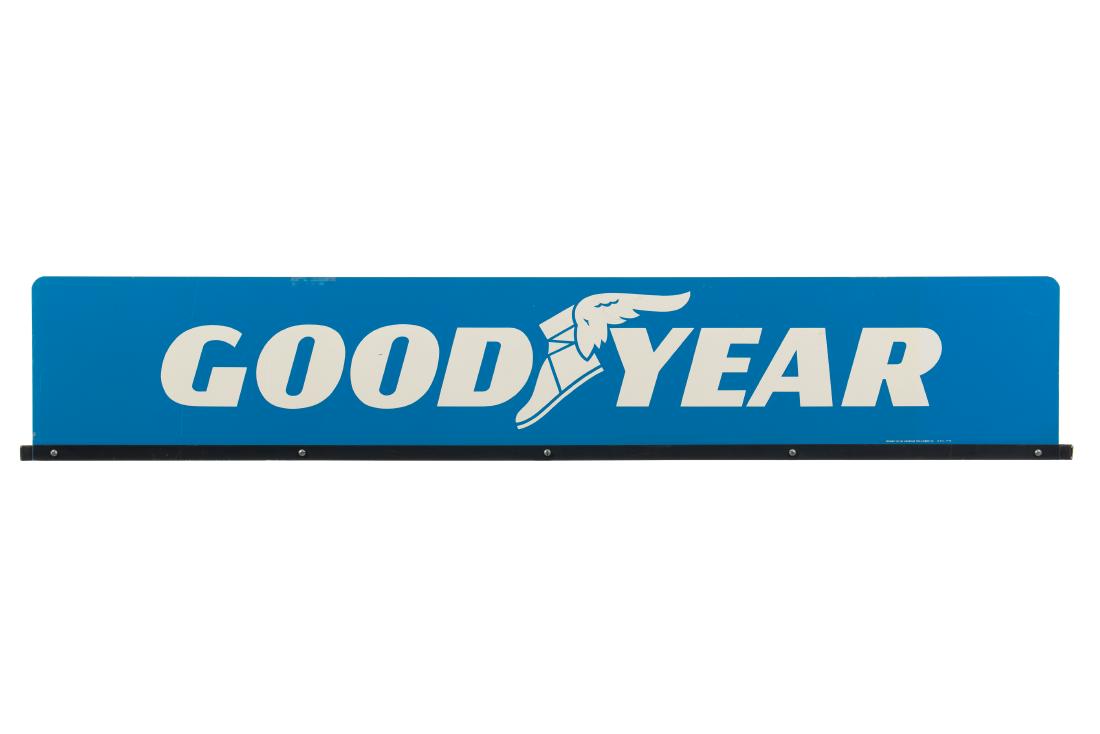 Goodyear Horizontal Tin Sign: DST. It has good color and gloss. It shows light wear, minor paint loss, and areas of slight discoloration. It displays well and is mounted on a square tubing bracket. Marked: Property Of The Goodyear