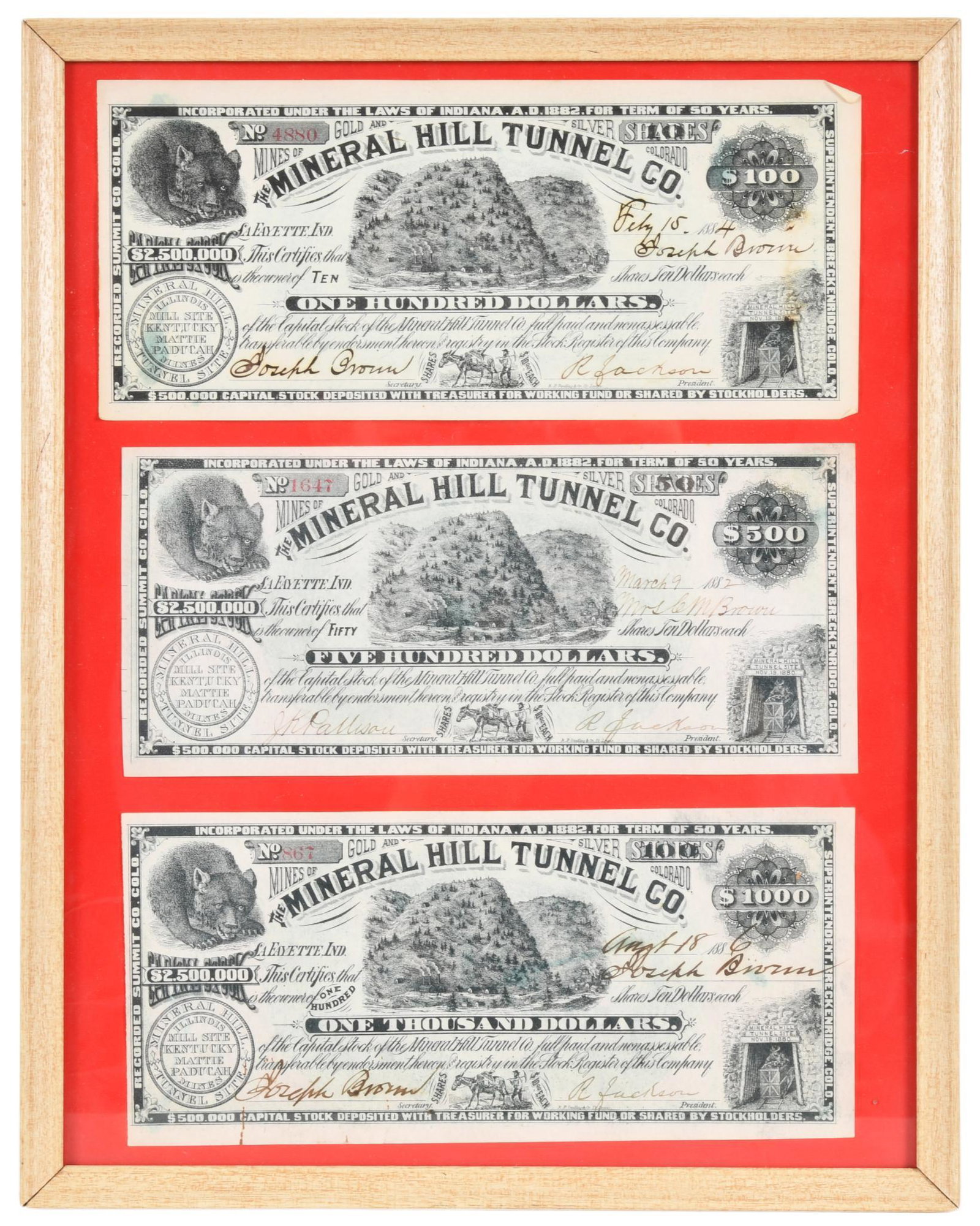 The Mineral Hill Tunnel Co. Capital Stock Certificates: 3 paper certificates in a frame, Lafayette, Indiana, $100, $500, and $1,000 certificates signed by the president and secretary of the company, dates range from 1882-1886, show wear, crease marks, and 