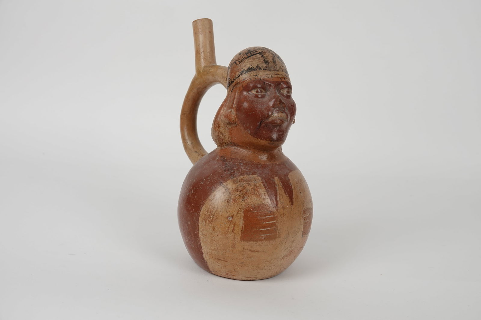 ARCHEOLOGIE: Vase à anse en étrier représentant un personnage. Visage grimaçant. N°167Cérmainque crème, brun-roiuge, noir.Hauteur : 24,5 cmLongueur : 20 cm Culture Mochica, ca 10
