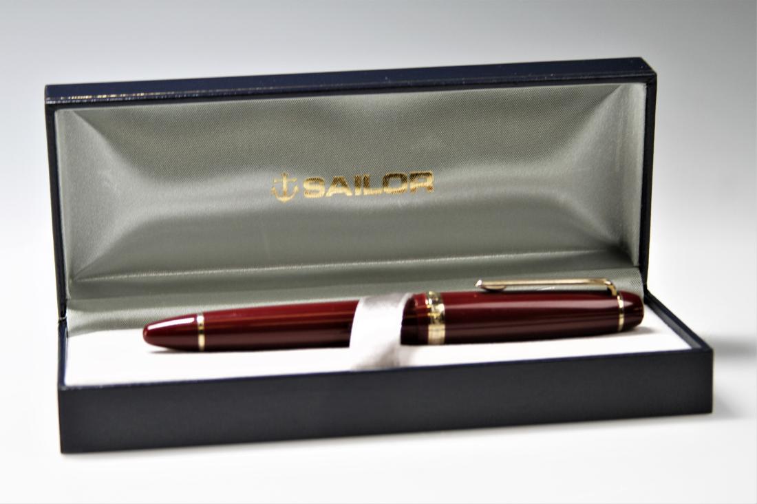 Sailor 1911 21kt Gold Nib Fountain Pen: Sailor "1911" red fountain pen. 21kt gold nib, clean intact; stamped "1911 21K Sailor H-M. Gold colored band on cap stamped "Sailor Japan Founded 1911." Includes original presentation box, 2 refills, 