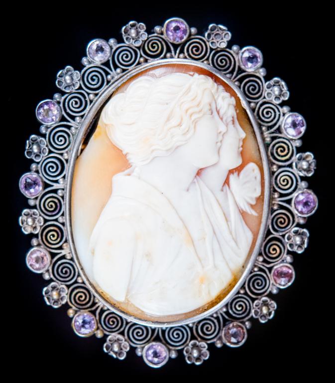 Antique Double Cameo Jeweled Silver Brooch: Item/Description: Rare, high relief, carved cameo of two beautiful women in profile. Ornate, pierced work lacy. Silver setting framed with pansies and lavender colored amethyst gemstones. Hinged pin w