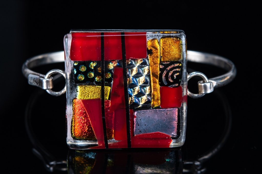 Signed Dichroic Glass Sterling Bangle: Item/Description: Studio art signed bracelet features glowing slice of dichroic glass bezel set in Sterling Silver frame; simple U shaped bangle with hook clasp. Engraved on back: R. Stokes in script.
