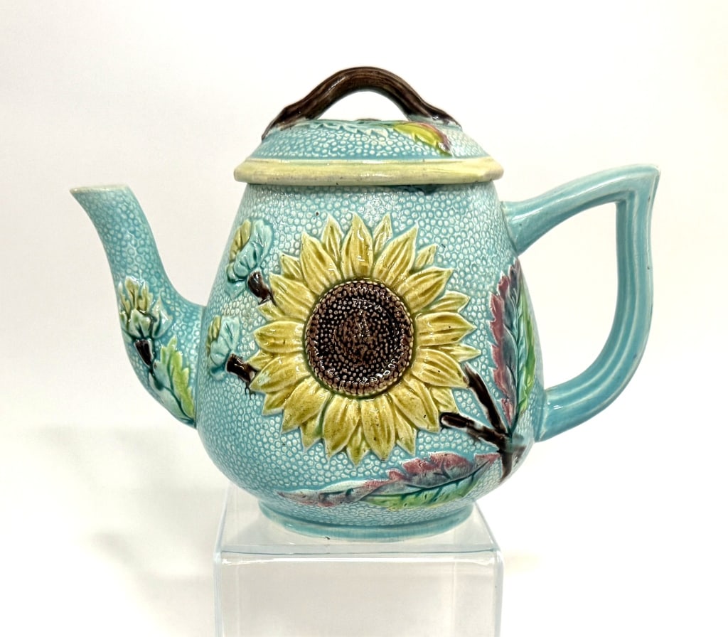 English Majolica Sunflower & Lily Teapot, 1880: Item/Description: Glazed Majolica teapot with embossed design. Features light blue textured background and floral motifs including Sunflowers and water lilies. Colorful glazes throughout. British Regi