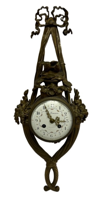 French Louis XVI Style Cartel Wall Clock: Item/Description: Decorative French cartel wall clock executed in the Louis XVI taste, featuring an ornate gilt bronze (ormolu) case with ribbon-and-bow crest, floral garlands, and scrolling foliate o