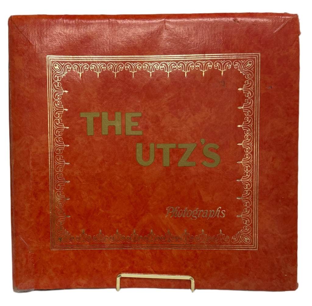 The Utz's Photographs Vintage Leather Photo Album: Item/Description: A vintage mid-20th century family photograph album titled "The Utz's", featuring a red faux-leather cover with gilt decorative border and lettering. The interior contains approximate