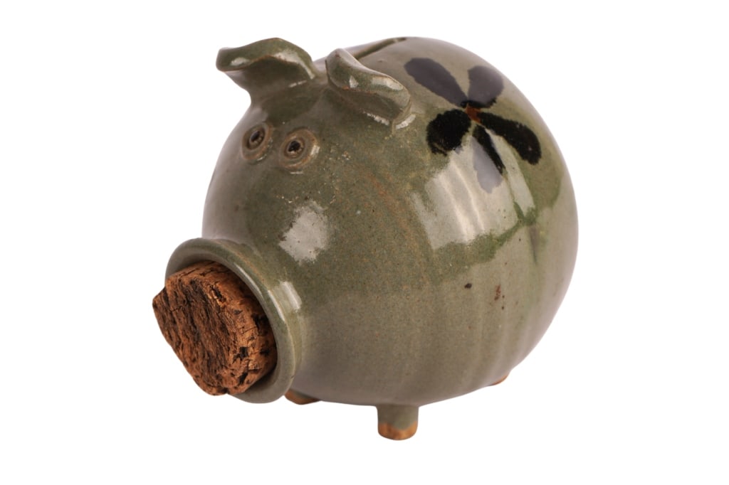 Glazed Stonewear Piggy Bank: Item/Description: Handcrafted ceramic piggy bank, featuring a greenish-grey glaze, whimsical dark floral pained designs, a cork stopper for the snout, and four small feet at its base. Material: