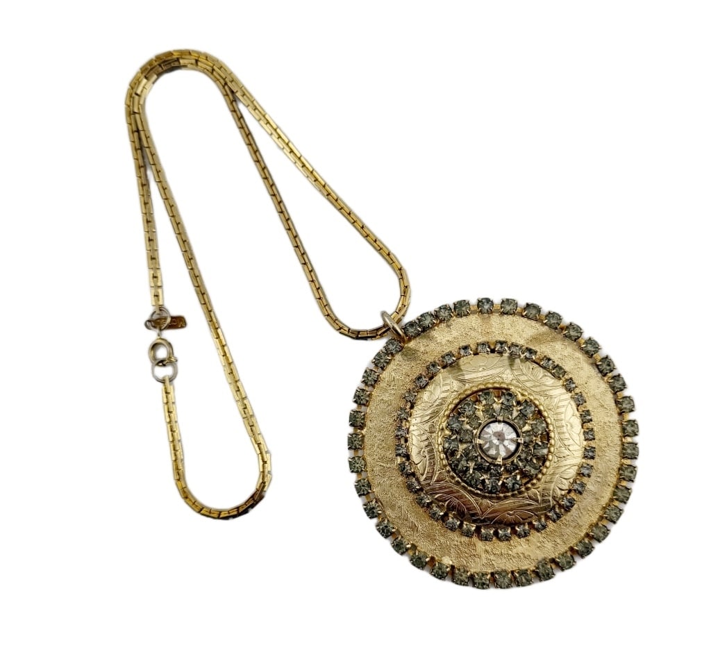 Monet Gold Tone Rhinestone Medallion Necklace: Item/Description: Bold signed statement medallion necklace by Monet. Large circular pendant in gold tone metal with brushed and textured surfaces embossed with flowers and scroll work. Concentric ring