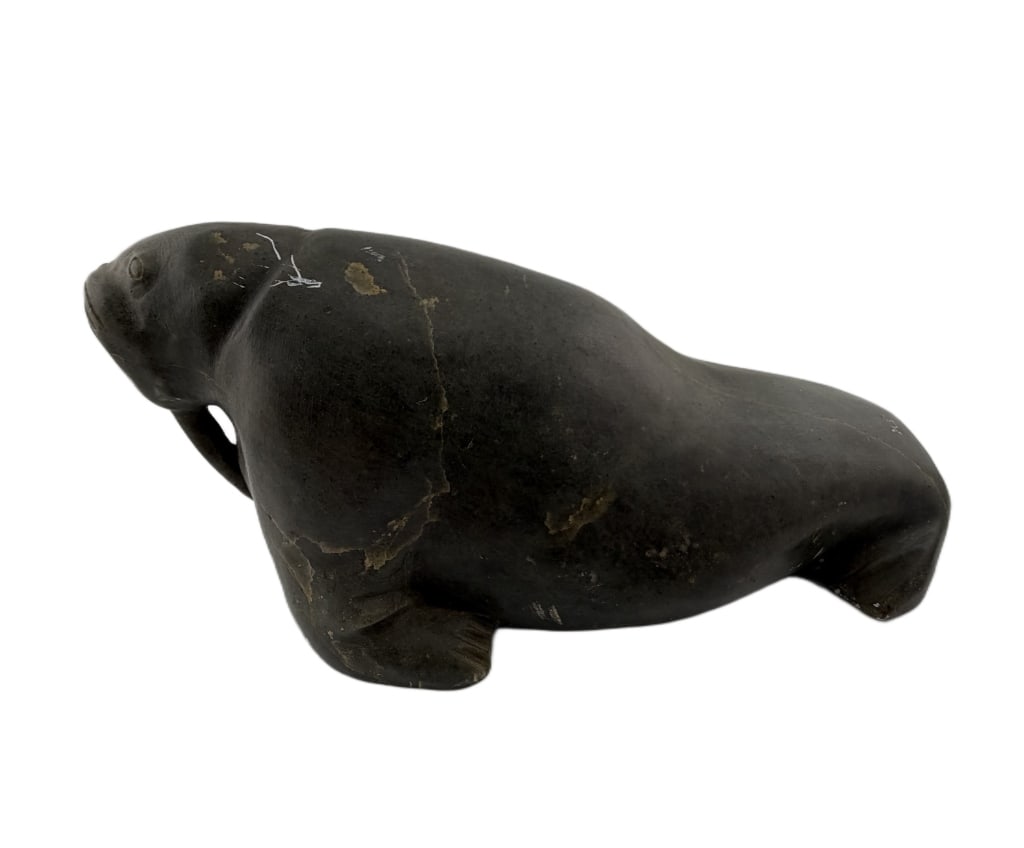 Inuit Hand-Carved Soapstone Walrus Sculpture: Item/Description: Hand-carved soapstone sculpture depicting a reclining walrus, showcasing naturalistic details including etched whiskers, prominent tusks, and a heavy, textured hide. Created by an